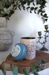 Çiçek desenli, mavili kapaklı pembe dekoratif metal kutu ahşap üzerinde