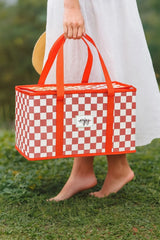 Kırmızı-beyaz kare desenli piknik sepeti, çıplak ayaklı beyaz elbiseli kadın tarafından taşınıyor