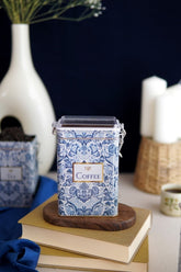 Mavi beyaz çiçek desenli kahve kutusu kitapların üstünde, arka planda mumlar ve çay kutusu