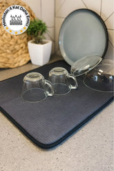 Mutfak tezgahında gri havlu kurutma matı ve ters çevrilmiş cam fincanlar ile tabaklar