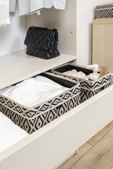 Desenli organize kutular içinde beyaz kıyafetler ve bakım ürünleri, üst rafta siyah şişme çanta