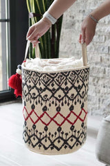 Kolları tutan ellerde kıl dokuma kırmızı ve siyah desenli beyaz çamaşır sepeti