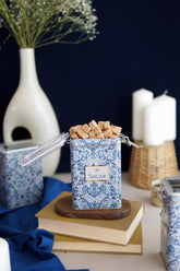 Mavi desenli şekerlik kutusunda küp şekerler, kitaplar ve dekoratif mumlar