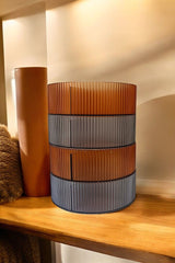 Ahşap rafta turuncu ve gri renkli, çizgili modern dekoratif lamba ve kahverengi silindir obje