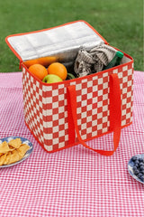 Kırmızı-beyaz kare desenli piknik soğutucu çanta, içinde meyve ve içecek, kırmızı ekose örtüde