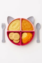 Kedili bölmeli pembe bebek mama tabağı, içi püre ve bisküvi dolu, gri kaşık ve çatal ile