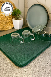 Yeşil bulaşık kurutma matsı üzerinde ters yerleştirilmiş cam bardaklar ve kapaklı çanak