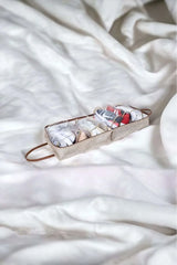 Beyaz ve renkli çorapların yer aldığı şeffaf kapaklı saklama kutusu, beyaz yumuşak kumaş üzerinde