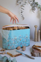 Mavi çiçekli ekmek kutusunda dilimlenmiş tahıllı ekmek ve ceviz, beyaz masa üzerinde