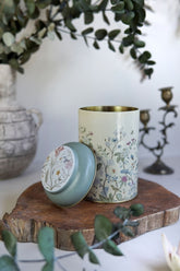 Çiçek desenli dekoratif metal kutu, ahşap yüzeyde, arka planda yapraklı dal ve antika şamdan