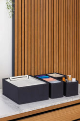 Dolap içi düzenleyici siyah kumaş kutular, içinde katlanmış beyaz tişört, renkli kıyafetler ve kozmetik şişeler