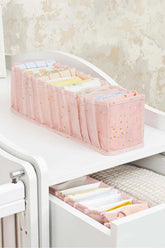 Pembe bölmeli düzenleyici içinde katlanmış bebek kıyafetleri ve beyaz mobilya çekmecesi