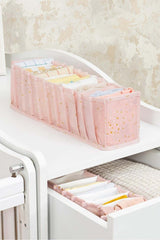 Pembe bölmeli düzenleyici içinde katlanmış bebek kıyafetleri ve beyaz mobilya çekmecesi