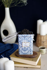 Mavi desenli kutuda kurutulmuş siyah çay, kitaplar ve beyaz dekoratif objelerle masa düzeni