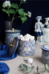 Mavi beyaz desenli kutuda marshmallowlar, arka planda porselen figürler ve yeşil çiçek