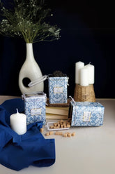 Mavi desenli kahve, çay ve şeker kutuları, beyaz mumlar ve dekoratif vazoyla masa düzeni