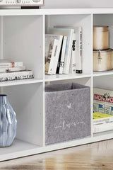 Beyaz kitaplıkta gri saklama kutusu, kitaplar, dekoratif mavi vazo ve metal kutular