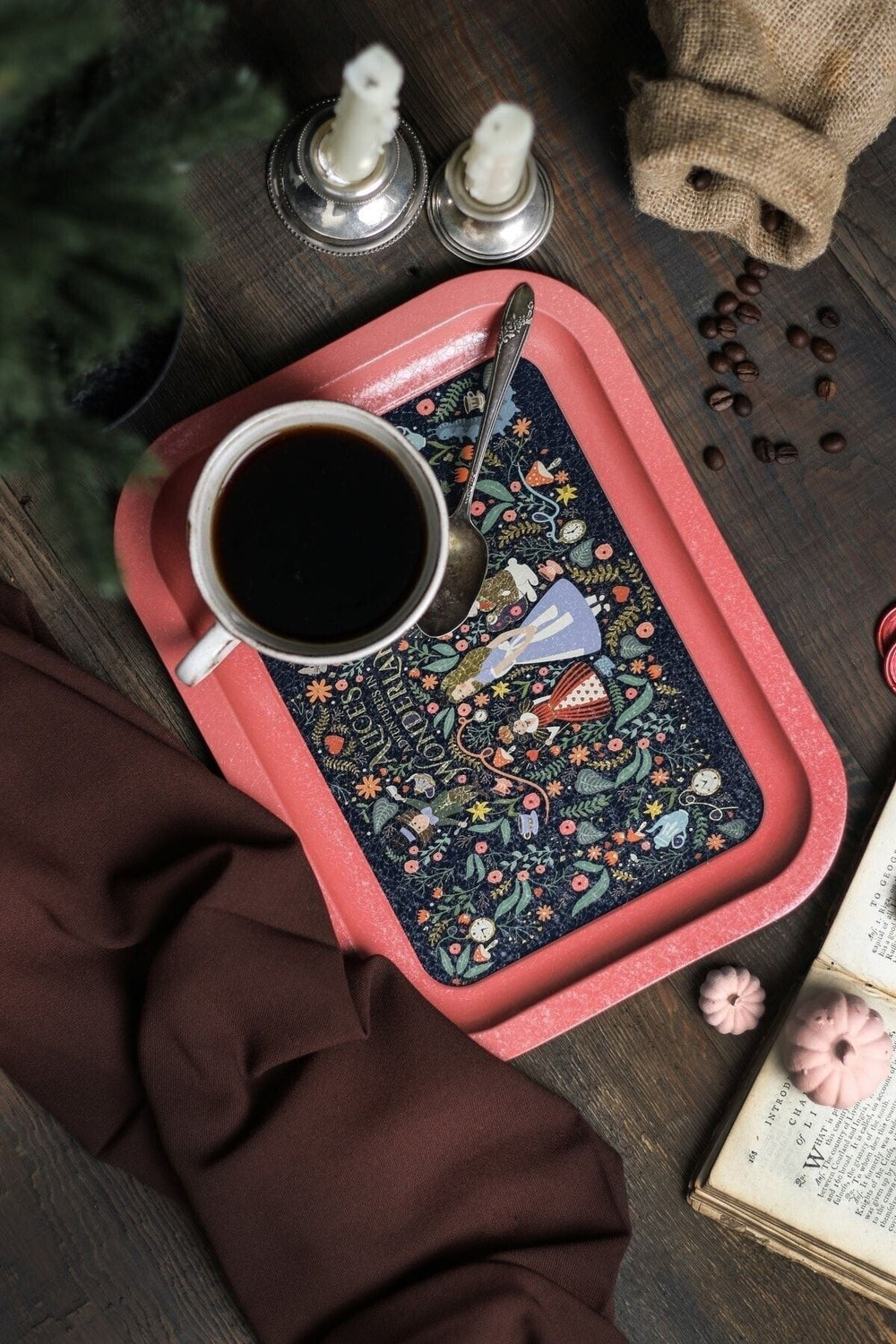 Alice Harikalar Diyarında desenli pembe tepsi üzerinde kahve fincanı, kahve çekirdekleri ve dekoratif mumlar