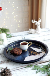 Kış temalı tepside kahve fincanı ve çam dallı iki kurabiye, arka planda beyaz geyik figürü