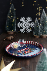 Kahverengi ahşap masada, kar desenli tepsi içinde küçük pipetli su bardağı ve renkli jelatinli şekerler