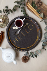 Kahverengi tepsi üzerinde beyaz kupa içinde siyah çay, iki beyaz şeker, gümüş kaşık, beyaz çaydanlık, dekoratif bitkiler ve tarçın çubukları