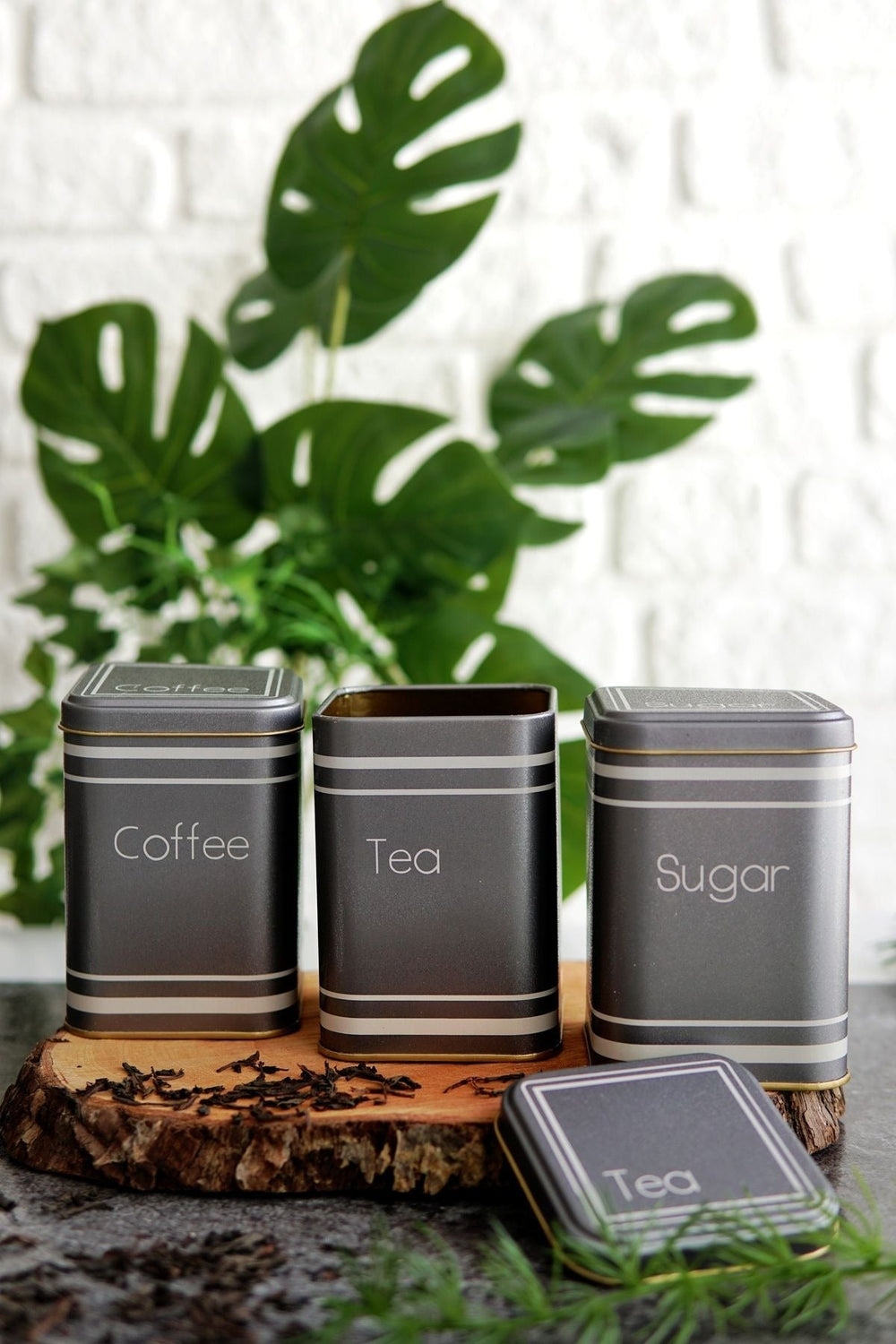 Kahve, çay ve şeker yazılı metal saklama kutuları, doğal ahşap yüzey ve yeşil bitkilerle