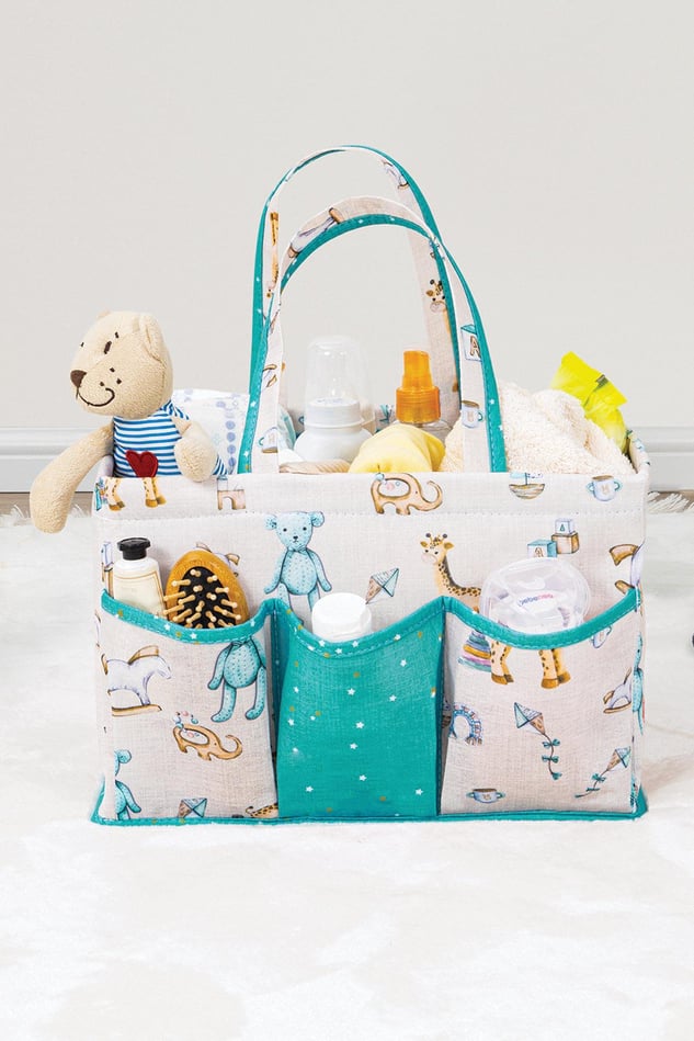Mavi desenli bebek bakım çantası içinde oyuncak ayı, şişe, tarak ve bebek bakım ürünleri