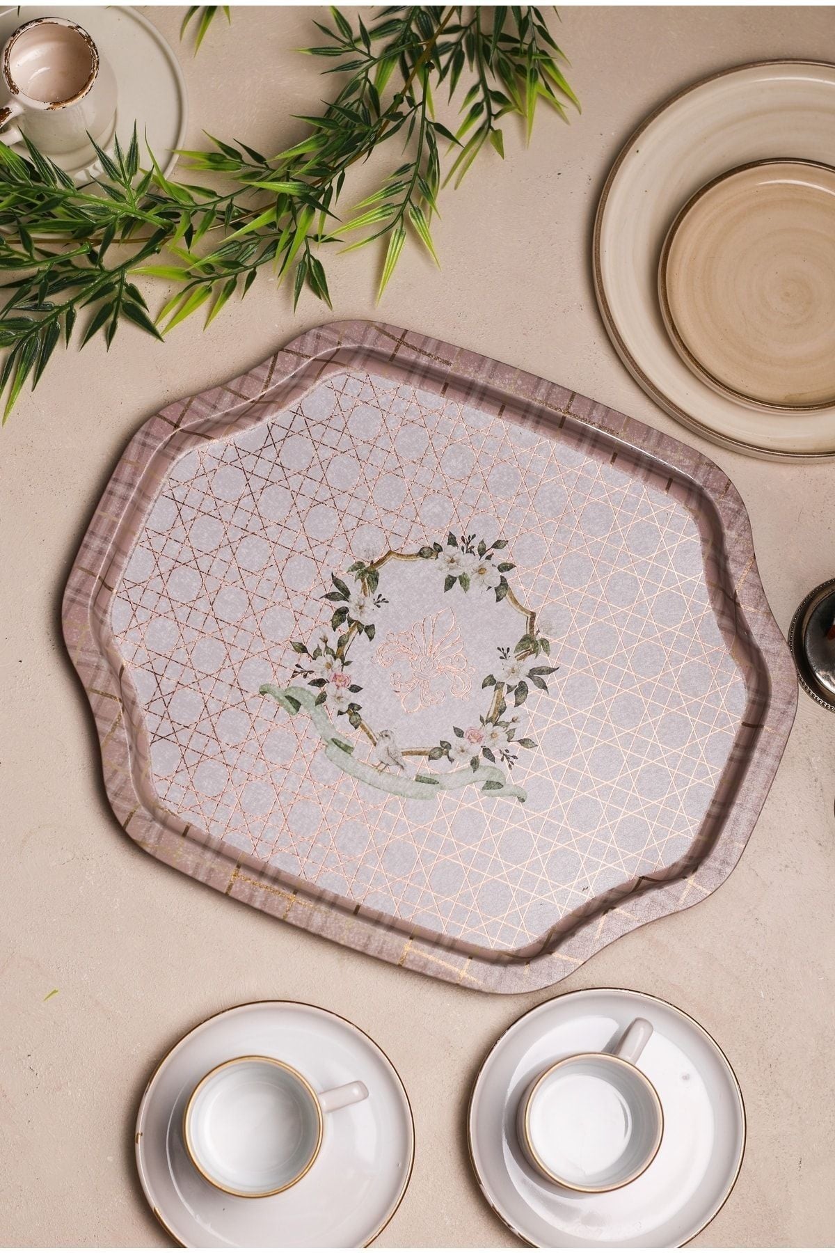 Çiçek ve kelebek desenli dekoratif servis tepsisi, beyaz kahve fincanları ve yeşil yapraklarla masa düzeni