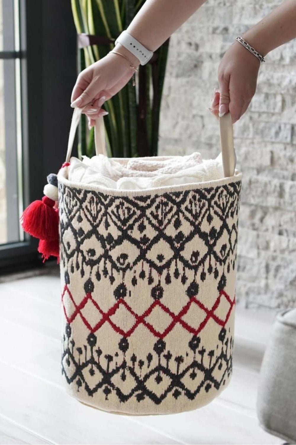 Kolları tutan ellerde kıl dokuma kırmızı ve siyah desenli beyaz çamaşır sepeti