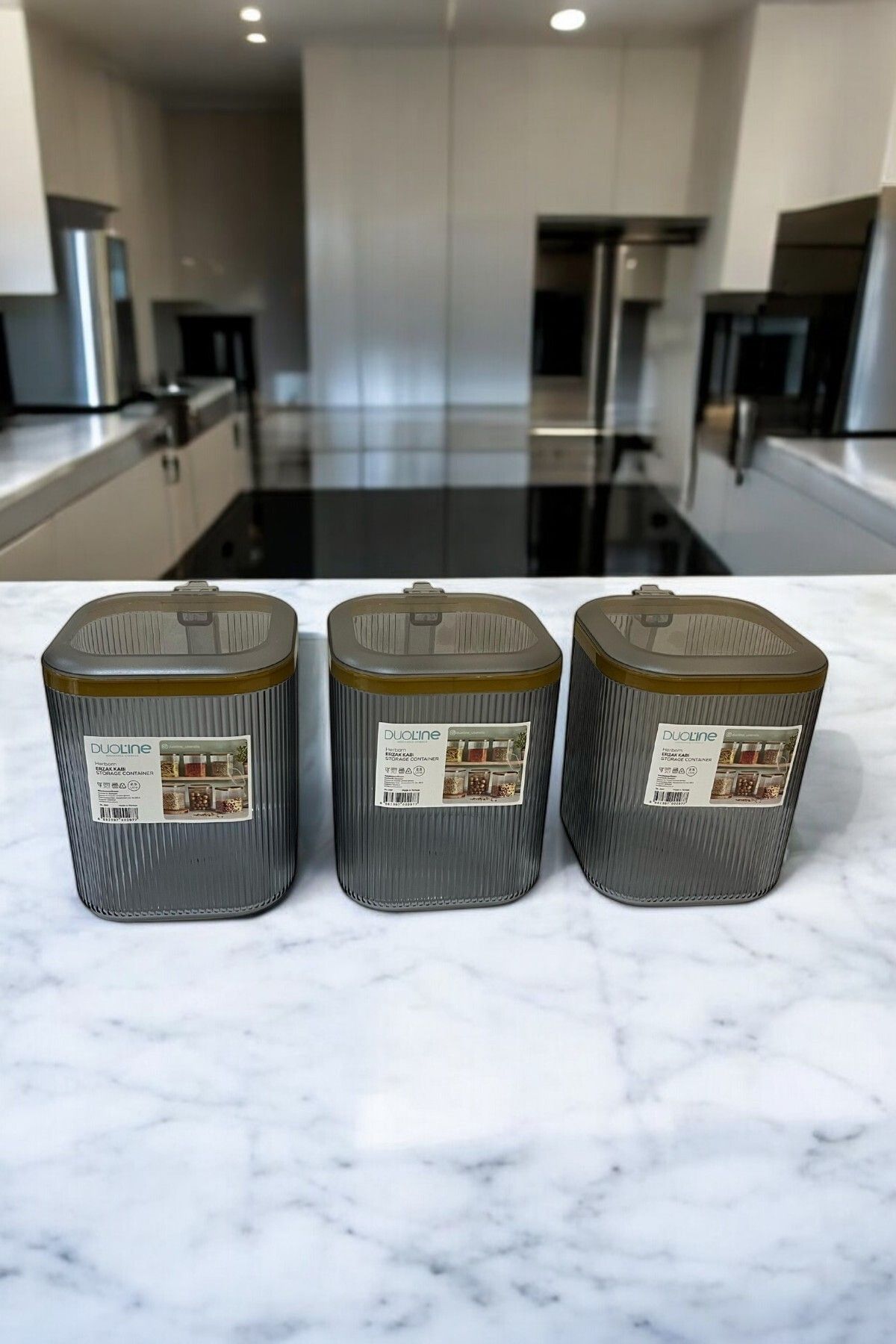 Mutfak tezgahında üç adet şeffaf Duoline saklama kabı, kare ve koyu renkli kapaklı