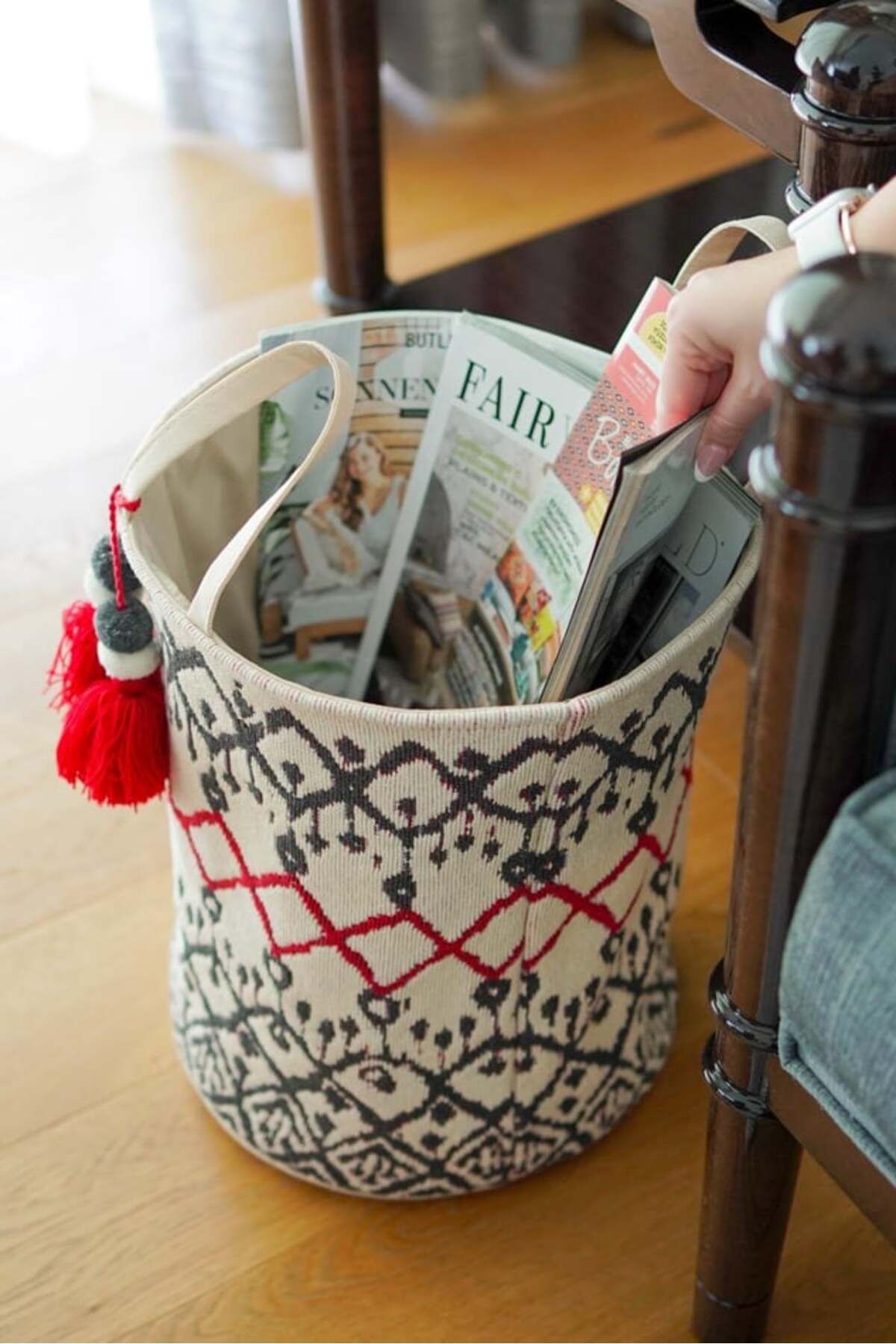Etnik desenli örgü dergi sepeti içinde çeşitli dergiler ve bir kişinin dergi alması
