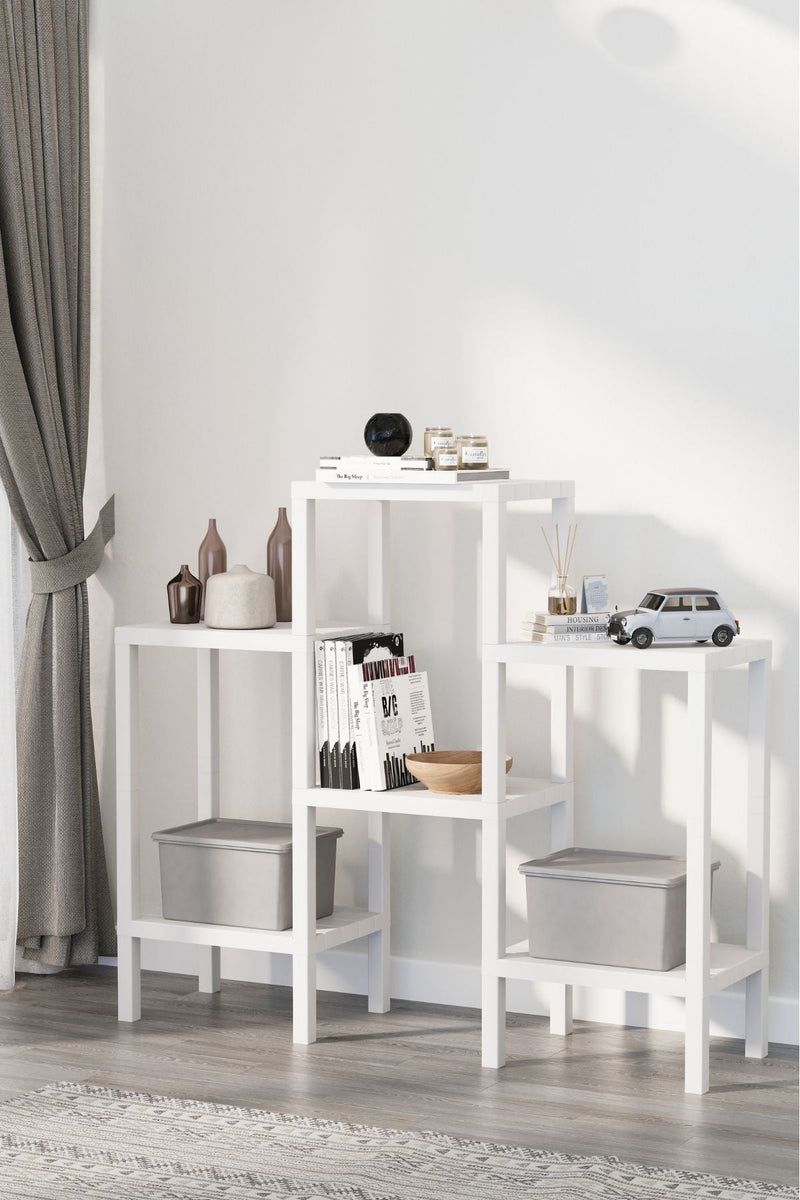 Beyaz modüler ev kitaplığı, kitaplar, dekoratif vazolar, mumlar ve minyatür arabanın yer aldığı modern oturma odası
