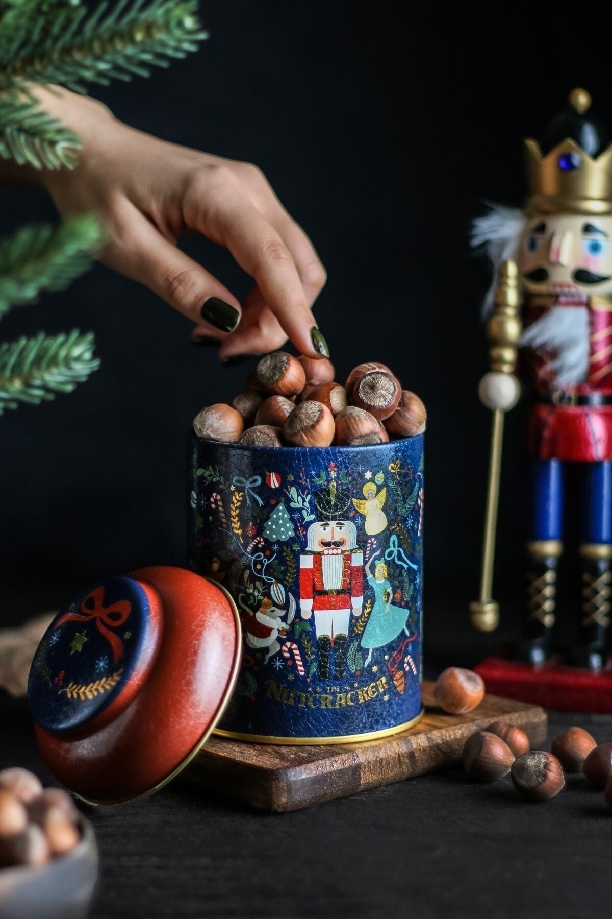 Fındık dolu Nutcracker temalı metal kutuya el uzanıyor, arka planda eğlenceli kurşun asker figürü