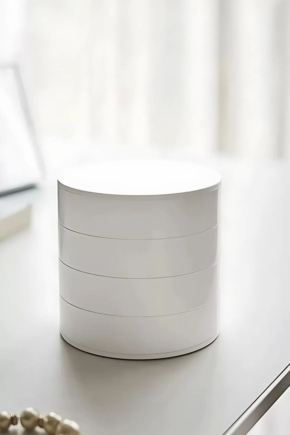 Minimalist beyaz yuvarlak kutu, modern masa üstünde, soft ışık ve dekoratif inci kolye