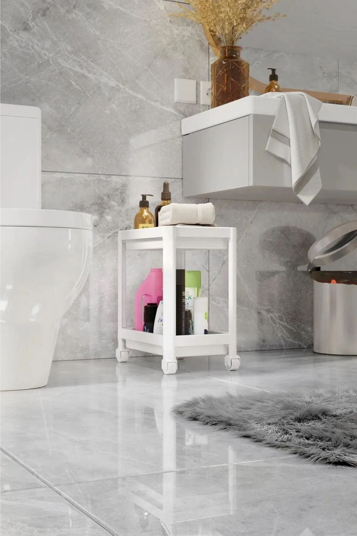 Gri mermer banyo zemininde beyaz tekerlekli banyo dolabı, havlu, şişeler ve beyaz klozet