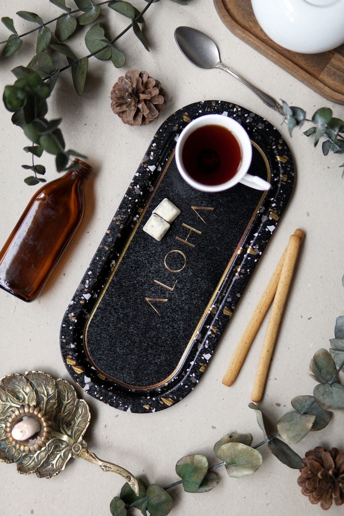 Violet harfli siyah terrazzo tepside çay fincanı, çubuk kraker, kahverengi cam şişe ve dekoratif objeler