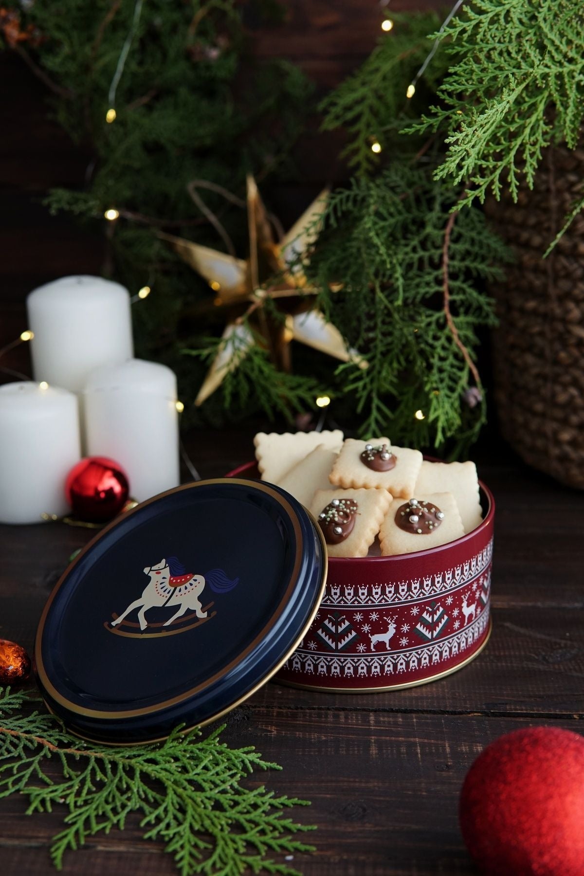 Kestane rengi masa üzerinde yılbaşı temalı kutuda süslemeli kurabiyeler, beyaz mumlar ve Noel dekorları