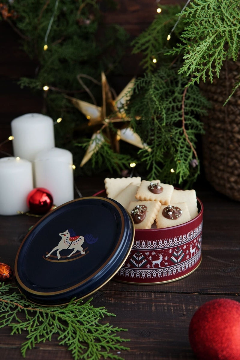 Kestane rengi masa üzerinde yılbaşı temalı kutuda süslemeli kurabiyeler, beyaz mumlar ve Noel dekorları