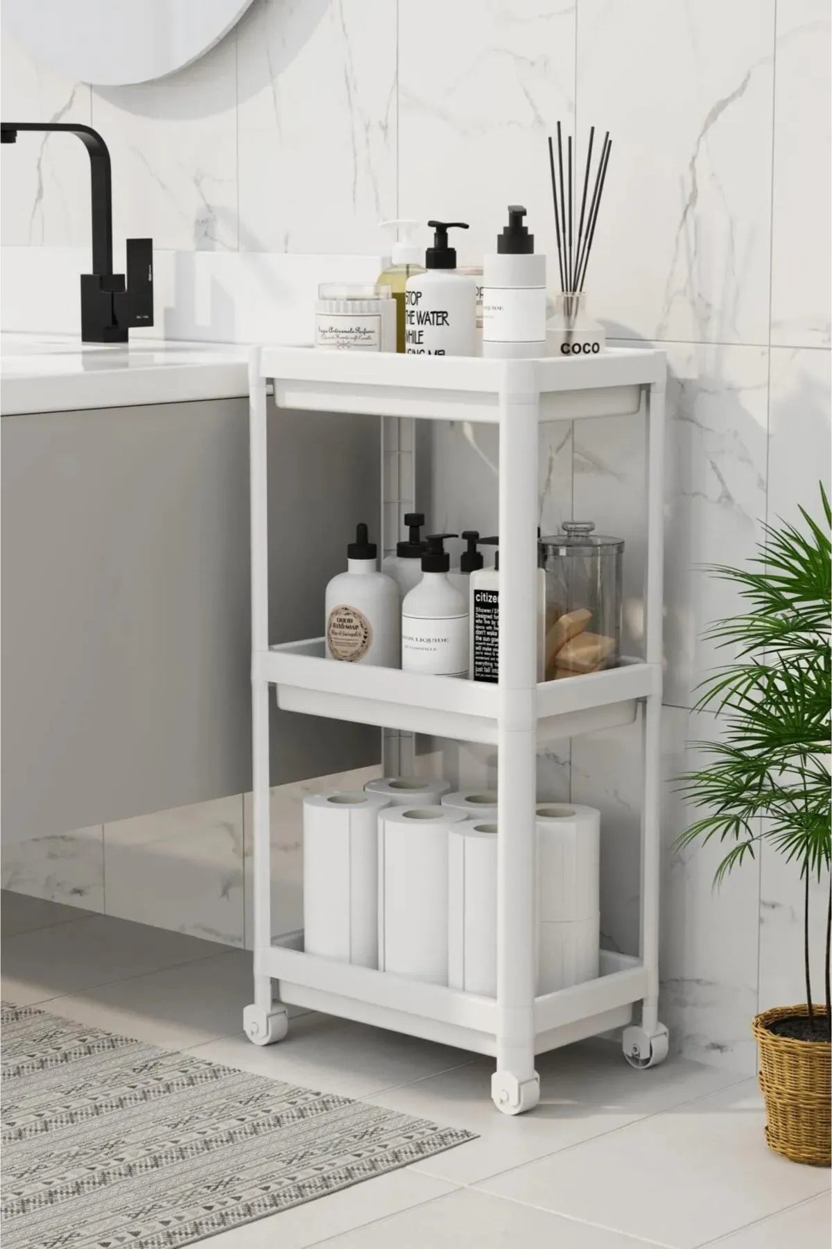 Beyaz tekerlekli banyo rafında şampuan, sabun ve tuvalet kağıtları, modern mermer duvarlı banyo