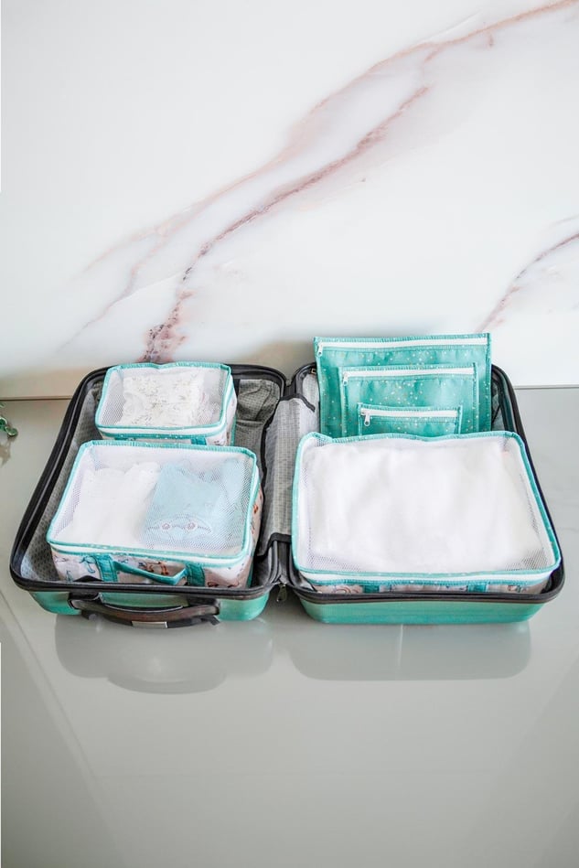 Mavi seyahat seti içinde düzenli bebek kıyafetleri ve organizer çantalarla açık valiz