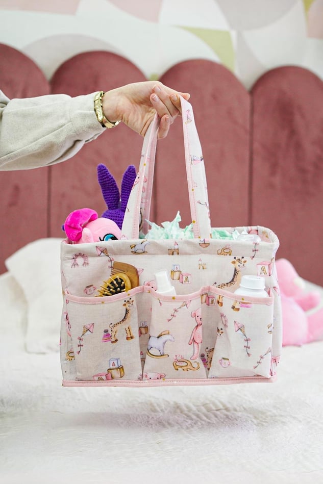 Pembe desenli bebek bakım çantası, dış ceplerinde tarak ve şişeler, içi oyuncak ve bebek malzemeleri dolu
