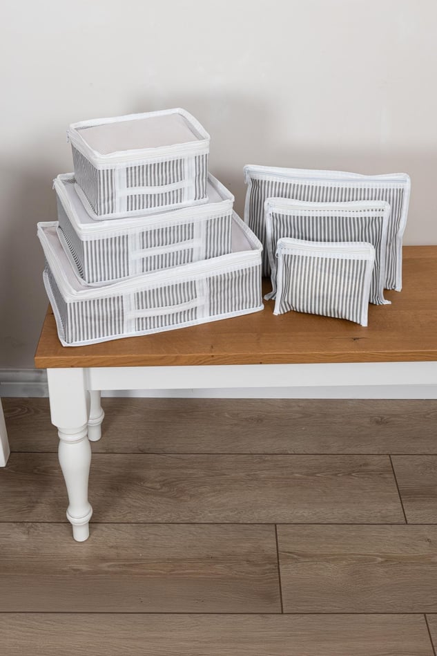Beyaz çizgili gri bavul organizer seti, beyaz masada ve ahşap zemin üzerinde
