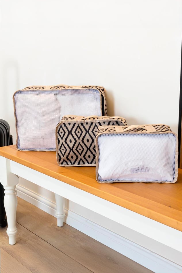 Ahşap üst yüzeyli beyaz sehpa üzerinde siyah desenli üç farklı boyutta seyahat çantası