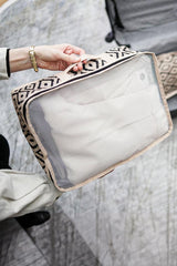 Kadın elinde siyah beyaz geometrik desenli şeffaf seyahat çantası tutuyor