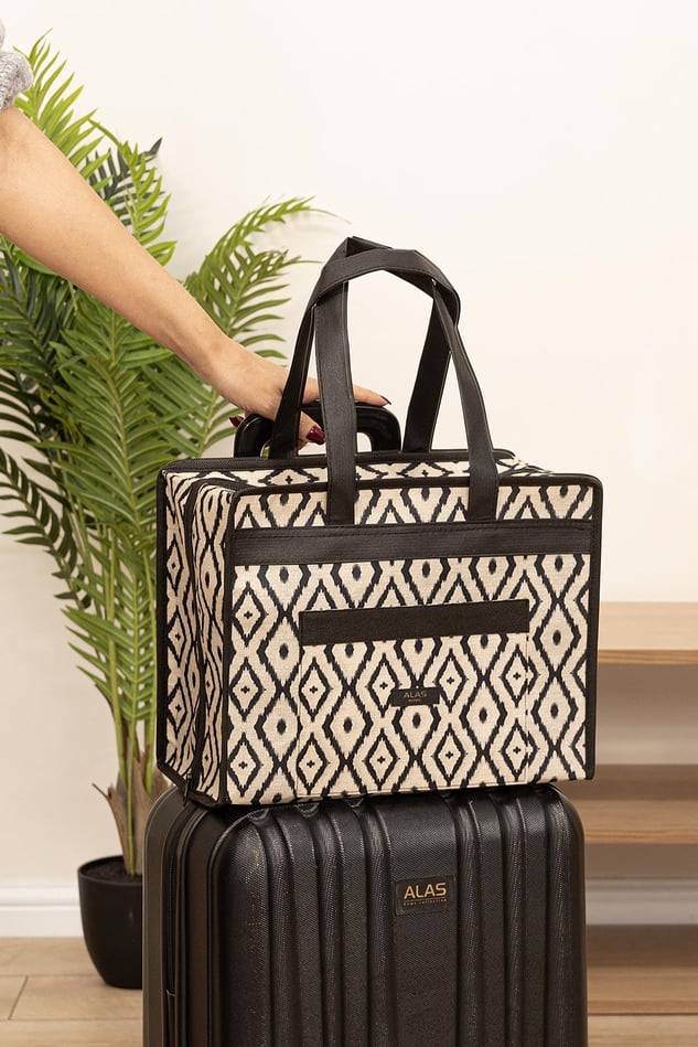 El tutmalı siyah beyaz geometrik desenli çok amaçlı seyahat çantası, siyah sert valizin üstünde
