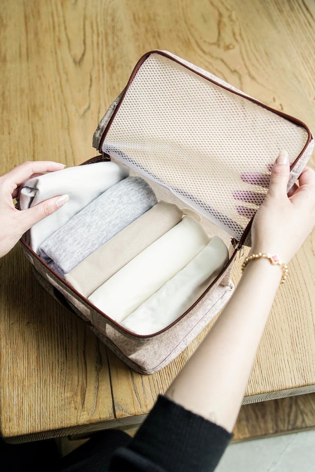 Ahşap masa üzerinde bej-renkli seyahat çantasında düzenli şekilde katlanmış açık renk giysiler