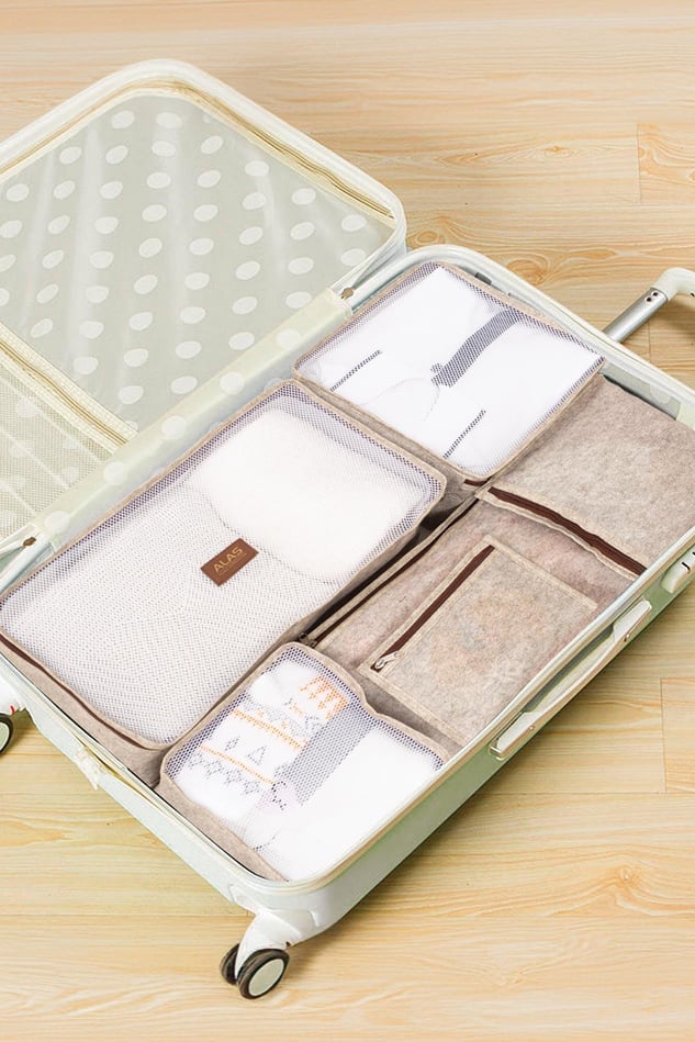 Açık yeşil sert kabuklu valizde düzenleyici bez çantalar ve seyahat eşyaları ile paketlenmiş