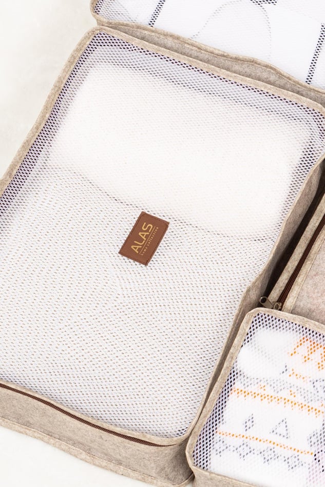 Bej seyahat çantası içinde iki farklı boyutta örgü seyahat organizeri, beyaz örtülerle